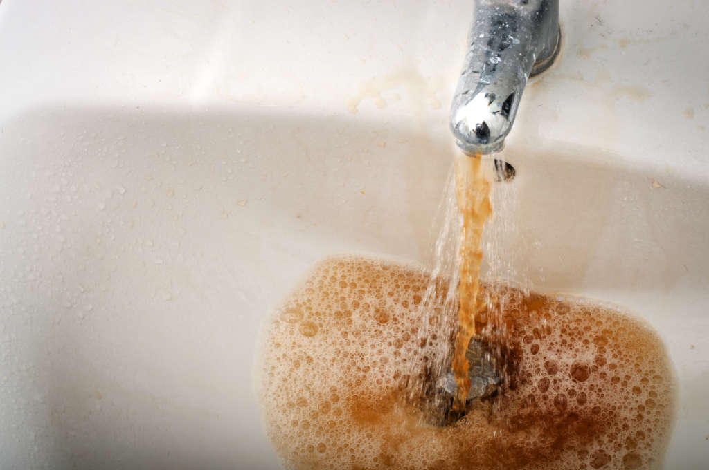 Grungy image of dirty brown water running from a water stained faucet