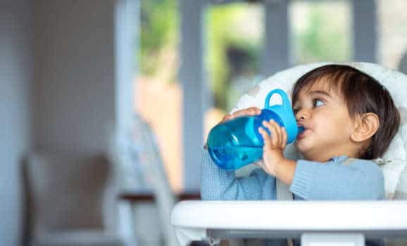 Baby in high chair drinking water