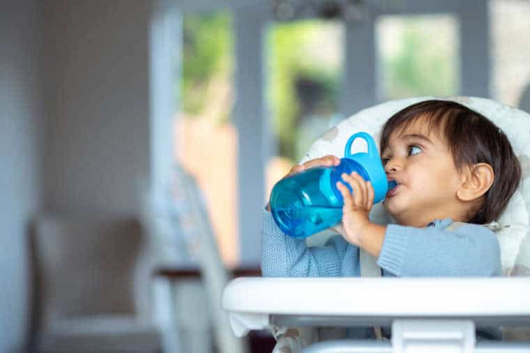 Baby in high chair drinking water