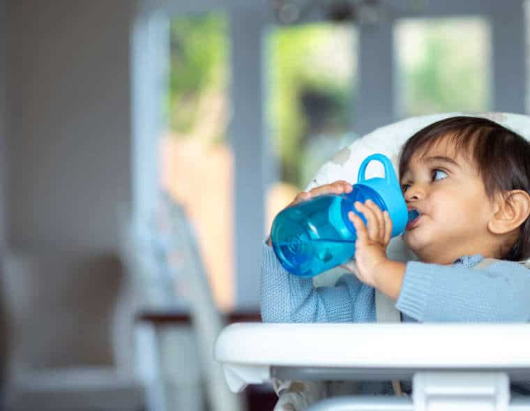 Baby in high chair drinking water