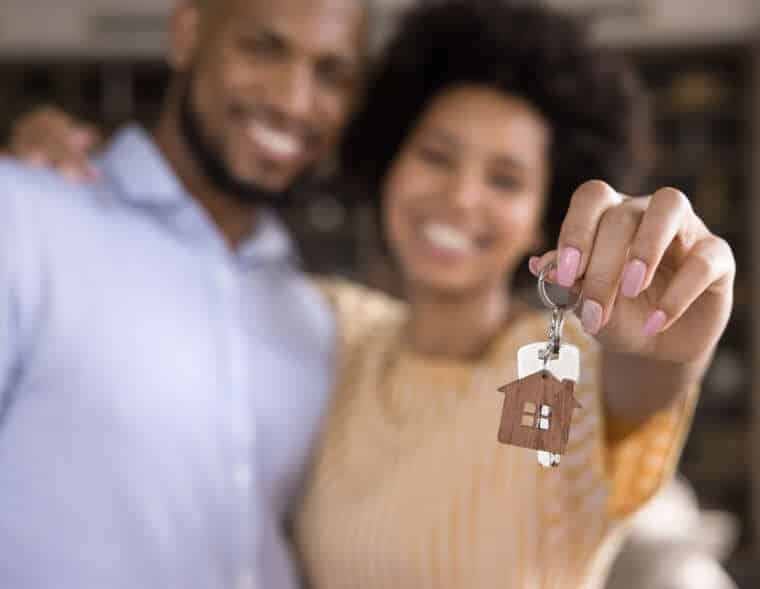 Close up focus on keys in hands of blurred joyful young loving married couple. Sincere homeowners celebrating purchasing own flat, feeling excited of renting new dwelling.