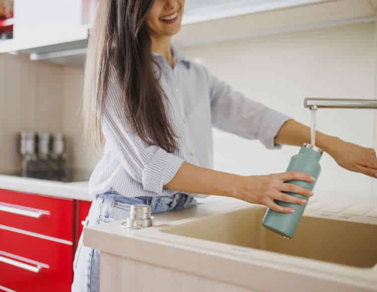 Close up of woman fills up reusable water bottle in the kitchen