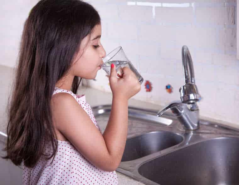 Little girl in the nice kitchen drinking water and smiling.