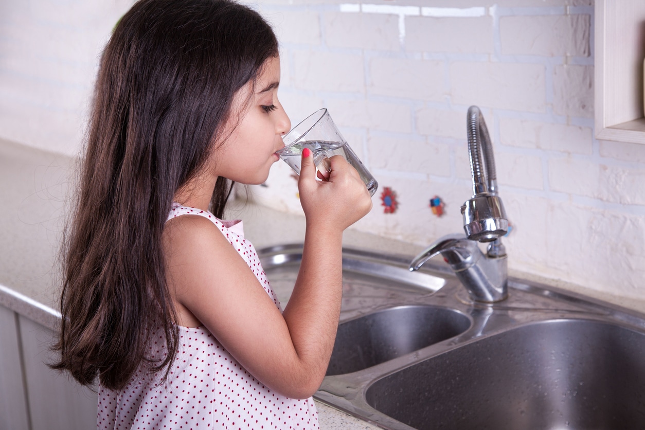 Little girl in the nice kitchen drinking water and smiling.