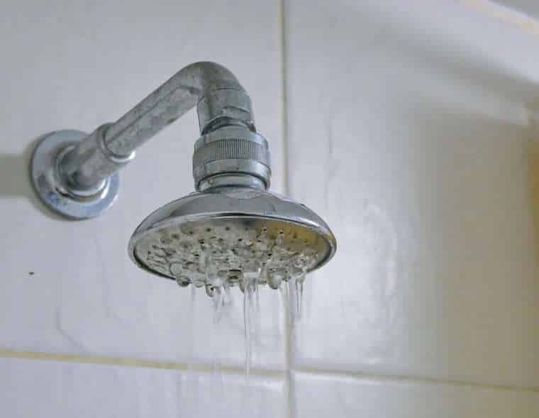 Close up of a partly clogged shower head in a bathroom, causing it to putting out so little water