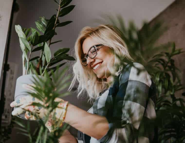 A happy woman enjoys time at her home, She waters one of her plant arrangements with a watering can.