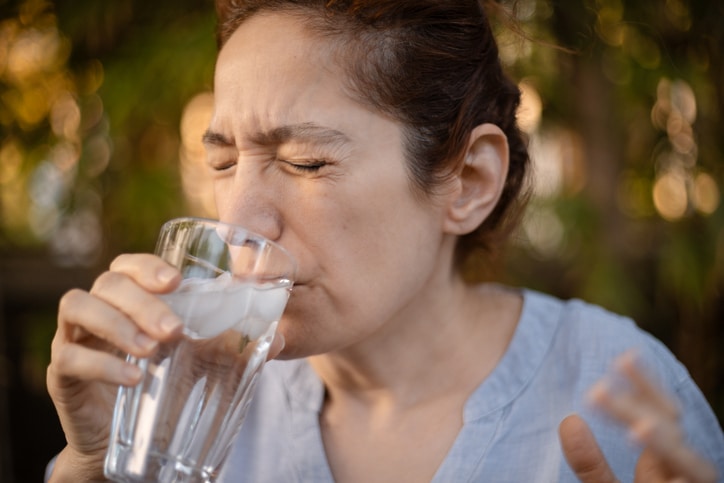 Caucasian woman reacting with tooth pain after taking a sip of ice cold water, part of a series