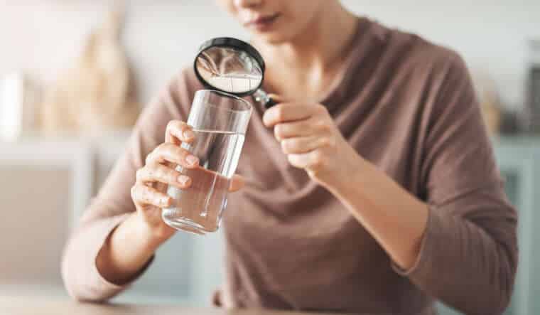 Woman looking at water in a glass through magnifying glass